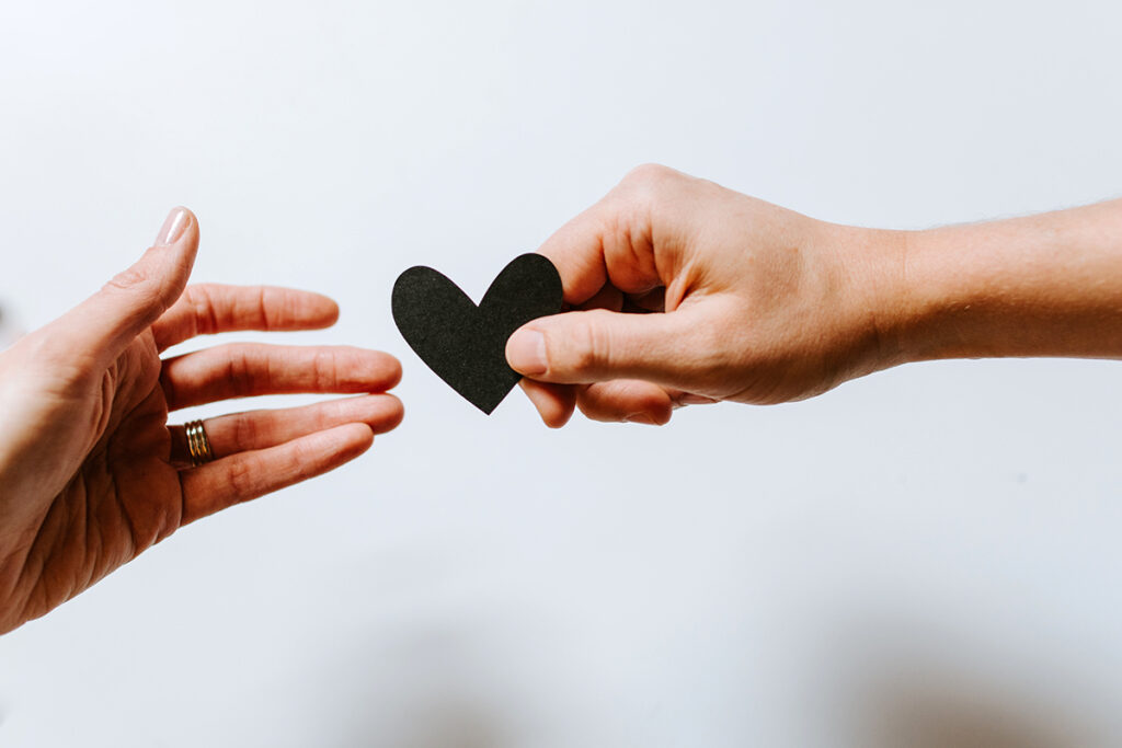 two hands exchanging black paper heart